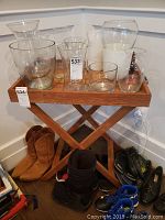 Wooden tray placed on foldable stand with various glass vases and pitchers on top. Tray and stand are wooden with natural wood finish.