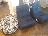 Photo showing two dark blue Xrocker gaming chairs with side speakers and one child size camouflage patterned beanbag chair next to them on the floor.