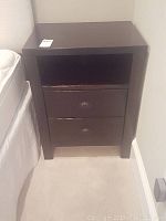Front view of one of the dark wood side tables showing the drawers and open shelf.