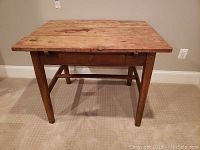Full frontal view of wooden office desk with one drawer and exposed wooden legs on carpeted floor.