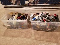 Two clear plastic bins filled with assorted LEGO pieces and partial builds.