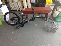 Full side view of the blue Novara Afterburner bike trailer with attached metal hook basket on concrete floor.