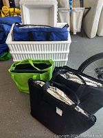 Three white styrofoam coolers stacked with lid, blue and black thermal insulated bags and grocery style insulated bags in black and green placed in front of coolers.