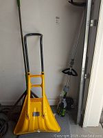 Photo of yellow deep mouth snow shovel and EGO cordless trimmer leaning against a wall