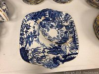 Top view of large square serving plate with smaller scalloped bowl centered on it, both with blue oriental designs and gold trim