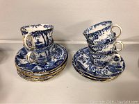 Photo of 5 teacups stacked on top of 10 saucers displaying the Blue Mikado pattern with blue oriental scenes, white base, and gold trim.