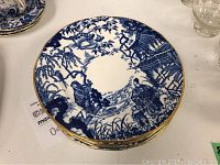 Top view of a single plate showing blue oriental scene and gold trim
