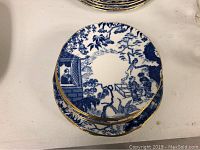 Top view showing blue oriental scene on white porcelain plate with gold trim edges.