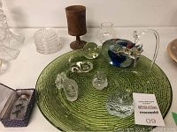 Overview of all items displayed including green glass plate, wooden goblet, stacked glass coasters, paperweight with hummingbird, glass figurines, and Chinese snuff bottle in box.