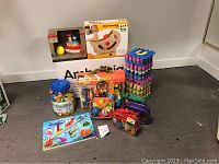 Photo showing all toys arranged against the wall with large Ambrosia box, foam floor tiles stacked, wooden puzzle, and various boxed toys