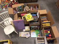 Boxes of assorted new and gently used children's books and two white toddler chairs visible.