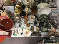 Overhead view of multiple pottery bowls, vases, glassware, Wade figurines and small decorative items arranged together on a table
