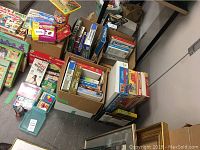 Wide view of assortment of games and puzzles in boxes and stacked on floor showing variety of products including Word Mastermind, Dominos, Jenga, and more.