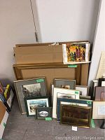 Collection of framed prints and a large gold frame arranged on floor against wall.