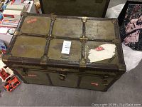 Closed vintage metal trunk with leather straps and metal reinforcements and locks. Some wear and stickers on top surface.