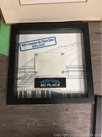 Framed square black shadowbox containing a metal piece labeled '100% Genuine BC Place Roof 1983-2010' with architectural drawing as background