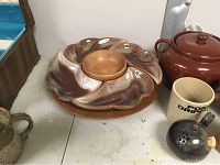Photo showing ceramic and teak swivel serving platter with removable dishes, brown ceramic lidded pot, a ceramic mug, and smaller ceramic containers on a table.