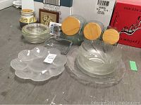 Top view of various clear glass platters and bowls, glass casseroles, dry goods storage containers with wooden lids, and glass tumblers in the background