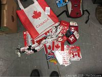 Photo of Canadiana merchandise including a Canada-themed tote bag, small flags, lanyards, pins, stickers, and other small memorabilia.