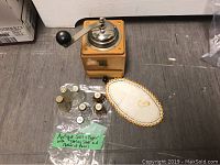 Photo showing wooden vintage Trosser coffee grinder with metal crank, six glass salt and pepper shakers with sterling silver and mother of pearl covers, and embroidered place mat with salt and pepper design.