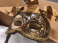 Close-up of brown masquerade mask with gold filigree, jester crown made of music note paper with small bells, and trimmed edges