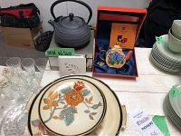 Photo showing cast iron teapot, Charlotte di Vita boxed teapot with iris design, Noritake plates, glassware and leaf coasters.