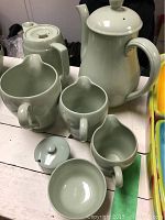 Tea set arranged on a table showing teapot, coffee pot, three creamers, and bowl, all green glazed ceramic.