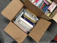 Cardboard box filled with various greeting cards stored standing upright, assorted sizes and types.