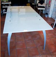 Full view of the white glass dining table with curved metal legs on tiled floor.