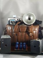 Brown leather camera bag with vintage cameras, flash unit, and blue ball set in front