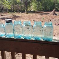 Photo of six vintage blue Ball mason jars, five quart-sized and one pint-sized, arranged on a wooden surface outdoors in daylight.