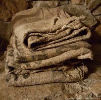 Stack of 4 used, folded burlap bags on stone surface