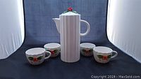Set of a ceramic coffeepot and four matching cups with Christmas holly decoration on white background.