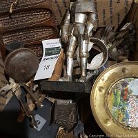 Photo showing assortment of vintage metal items including a knight metal figurine, cast iron cornbread pan, and other metal tools and utensils inside a box
