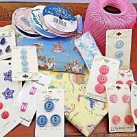 Assorted buttons on cards, rolls of ribbons, and baby fabric pieces in pink and blue