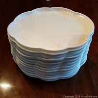 Stack of 12 white milk glass snack plates showing scalloped edges and embossed grape motif on rim.