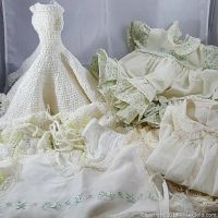 Full lot of assorted white vintage doll clothes displayed against a white backdrop showing multiple dresses and garments with lace and delicate details.
