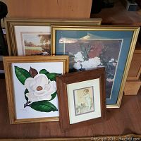 Lot of 4 framed decor prints leaning against furniture showing all items together.