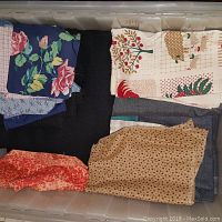 Photo of assorted fabric pieces neatly folded inside a large plastic tub, showing various prints and colors including floral and holiday patterns.