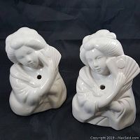 Front view of two white ceramic tiki mugs shaped as geisha girls holding fans.