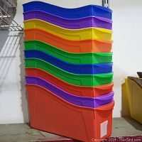 Stack of assorted colored plastic bins showing wave-shaped front edges, aligned for stacking and interlocking.