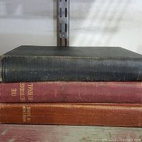 Three hardcover hymnals stacked; one black, one dark red, one brownish-orange, showing titles.