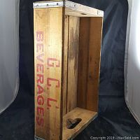 Photo showing rectangular wooden beverage crate with metal corner reinforcements and 'G.C.L. BEVERAGES' printed in red on the side.