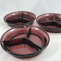 Three vintage purple glass divided dishes arranged in a triangular formation, showing the side and top view of the dishes. Each dish has three separate compartments.