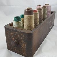Side angled view of a wood drawer with eight different colored thread cones