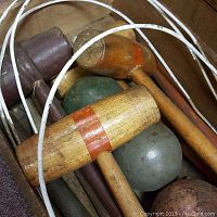 Close-up of wooden croquet mallets with colored bands and wooden balls inside wooden box.