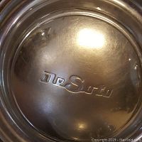 Close-up photo of one silver metal De Soto hubcap showing center embossed De Soto script logo and surface scratches.