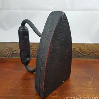 Front angled view of the cast iron sad iron on a wooden surface showing its shape and handle.