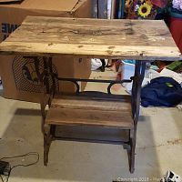 Side view of rustic table showing rusted sewing machine metal base and rough cut wooden top surface with natural wear and marks.