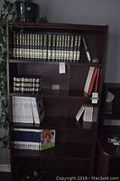Full bookcase showing multiple shelves with various books including black and navy hardback World Book encyclopedias, and colorful children's books.
